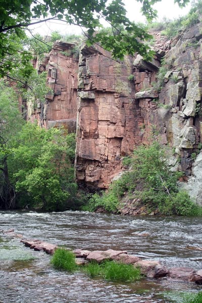 A red sandstone cliff rising straight out of the St. Vrain at the Planet Bluegrass ranch